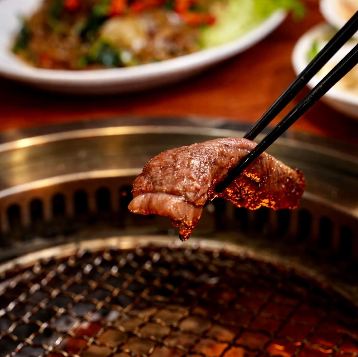 焼肉網の上で焼いた肉を箸で持ち上げているクローズアップ写真