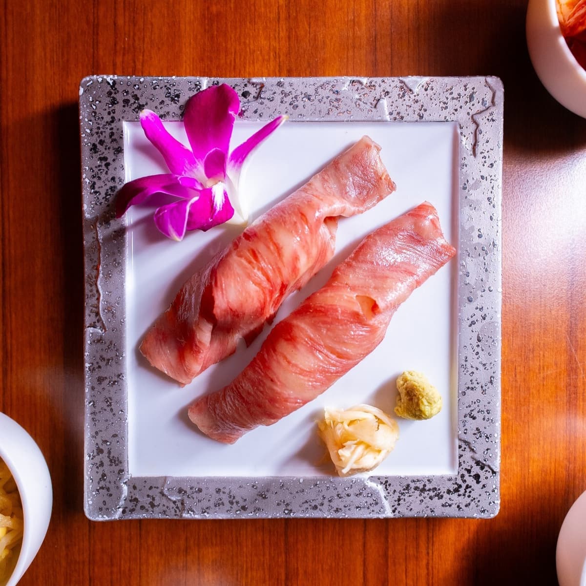 白い角皿に盛られた炙り肉寿司とガリ、わさび、花飾り