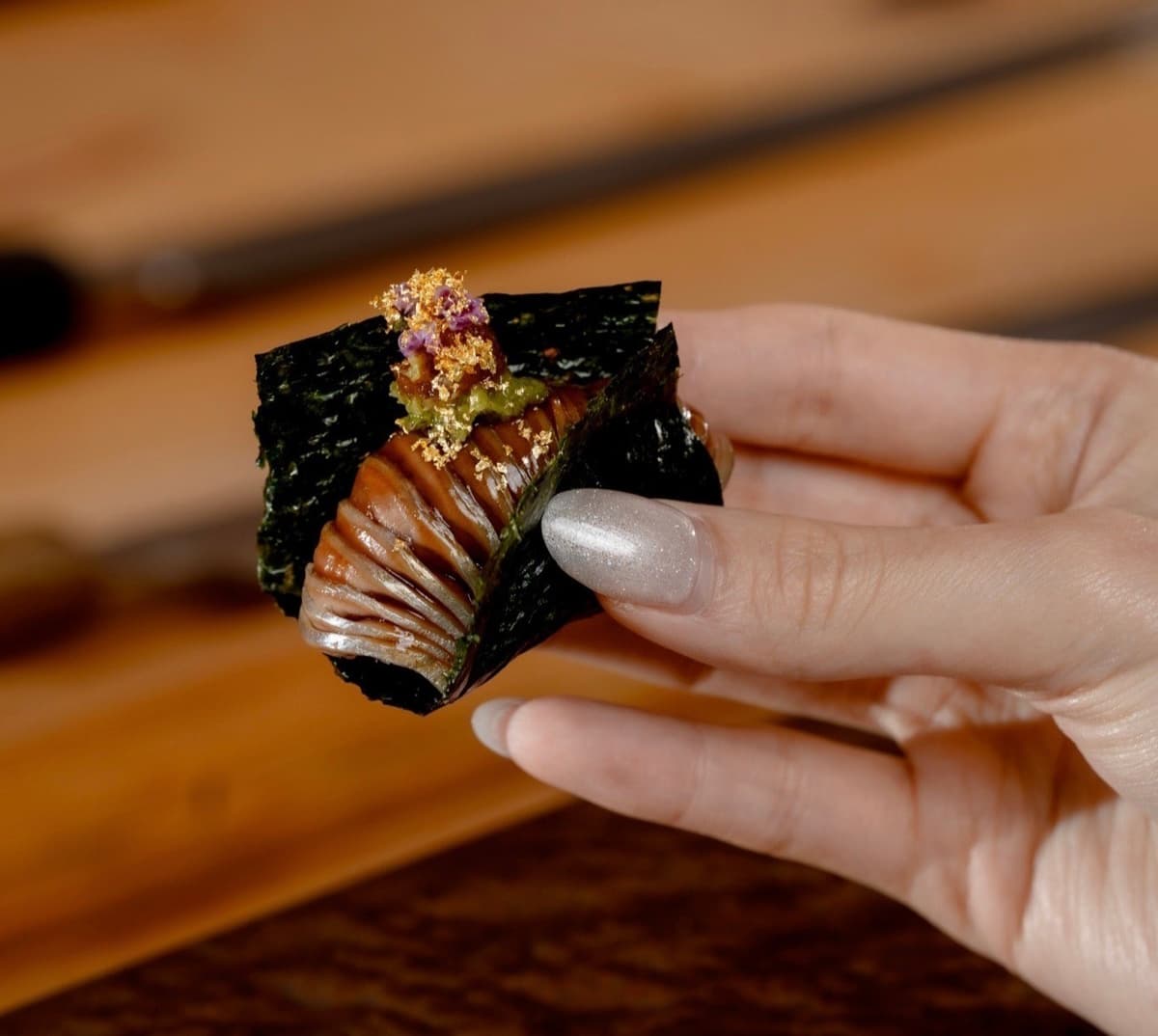 手に持った海苔巻きに炙り魚と薬味をのせた寿司ロール