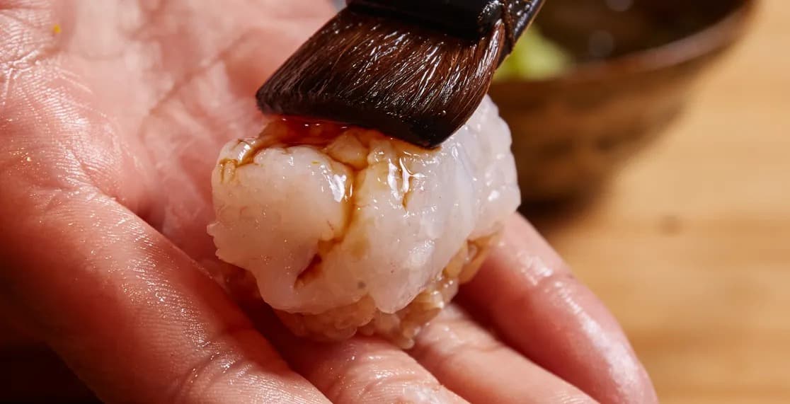 手のひらにのせた海老の握りに刷毛でタレを塗る様子
