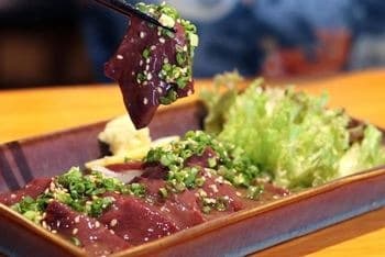 ごまと青ねぎをまぶしたレバー料理を箸で持ち上げる様子