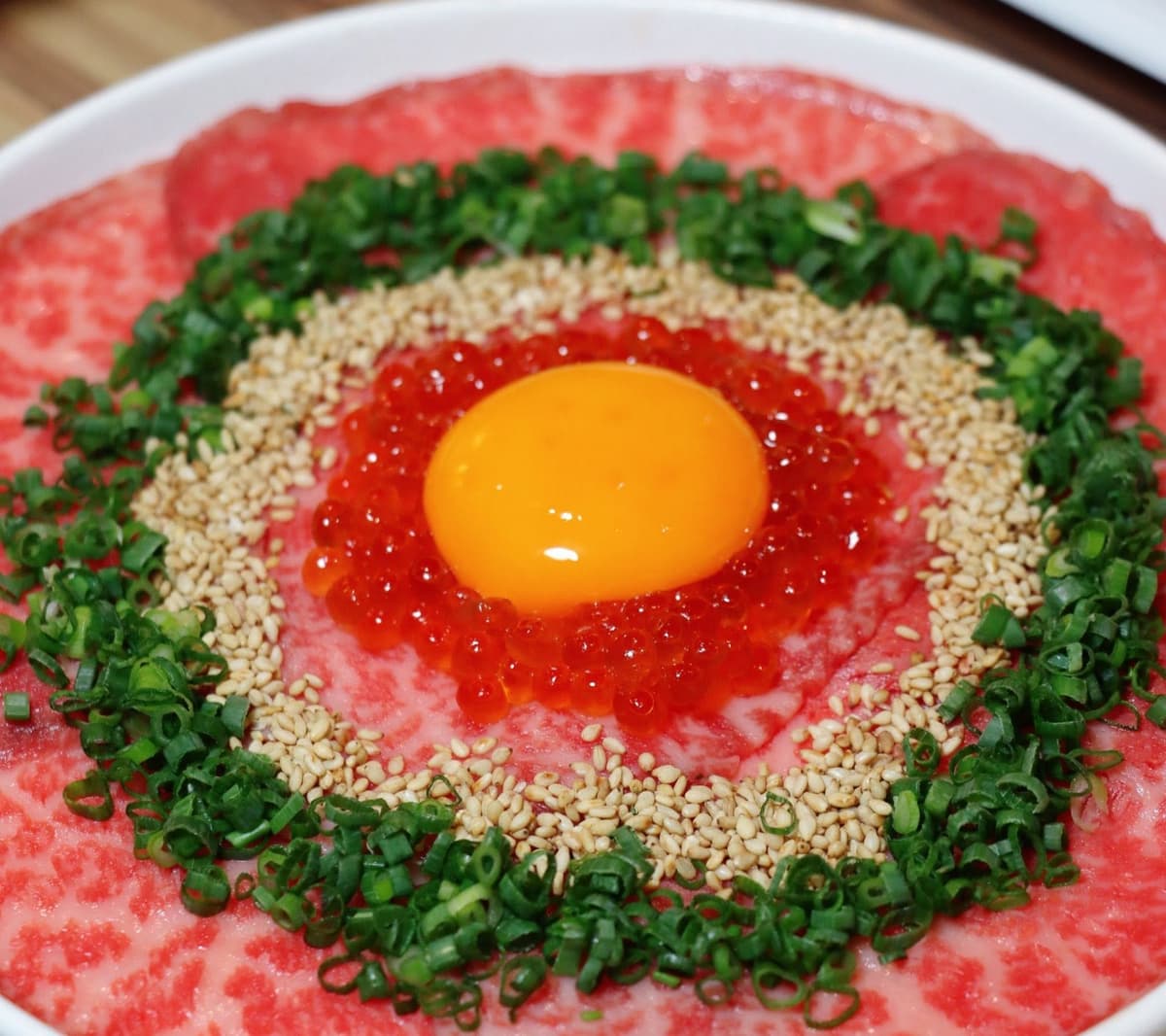 薄切り牛肉に卵黄、イクラ、白ごま、青ねぎを盛り付けた料理