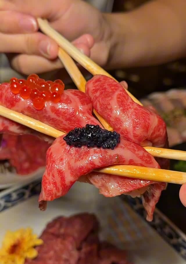 イクラや黒い魚卵をのせた霜降り牛肉の握りを箸で持つ様子