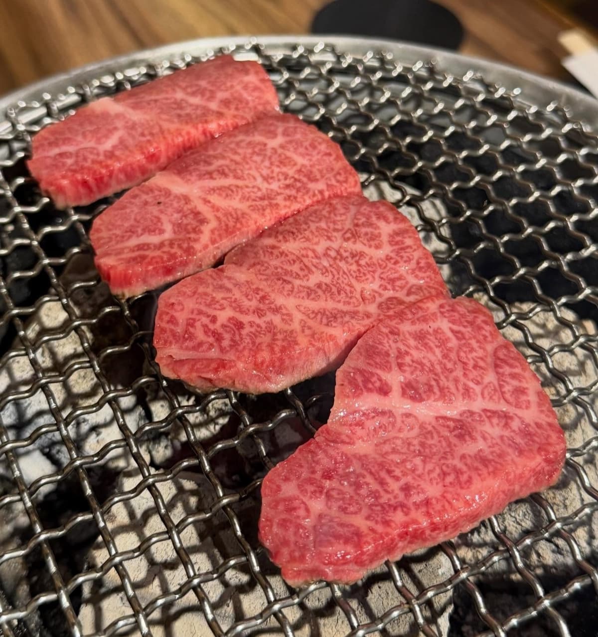 炭火焼きの網に並べられた、きめ細かな霜降り牛肉の厚切り肉