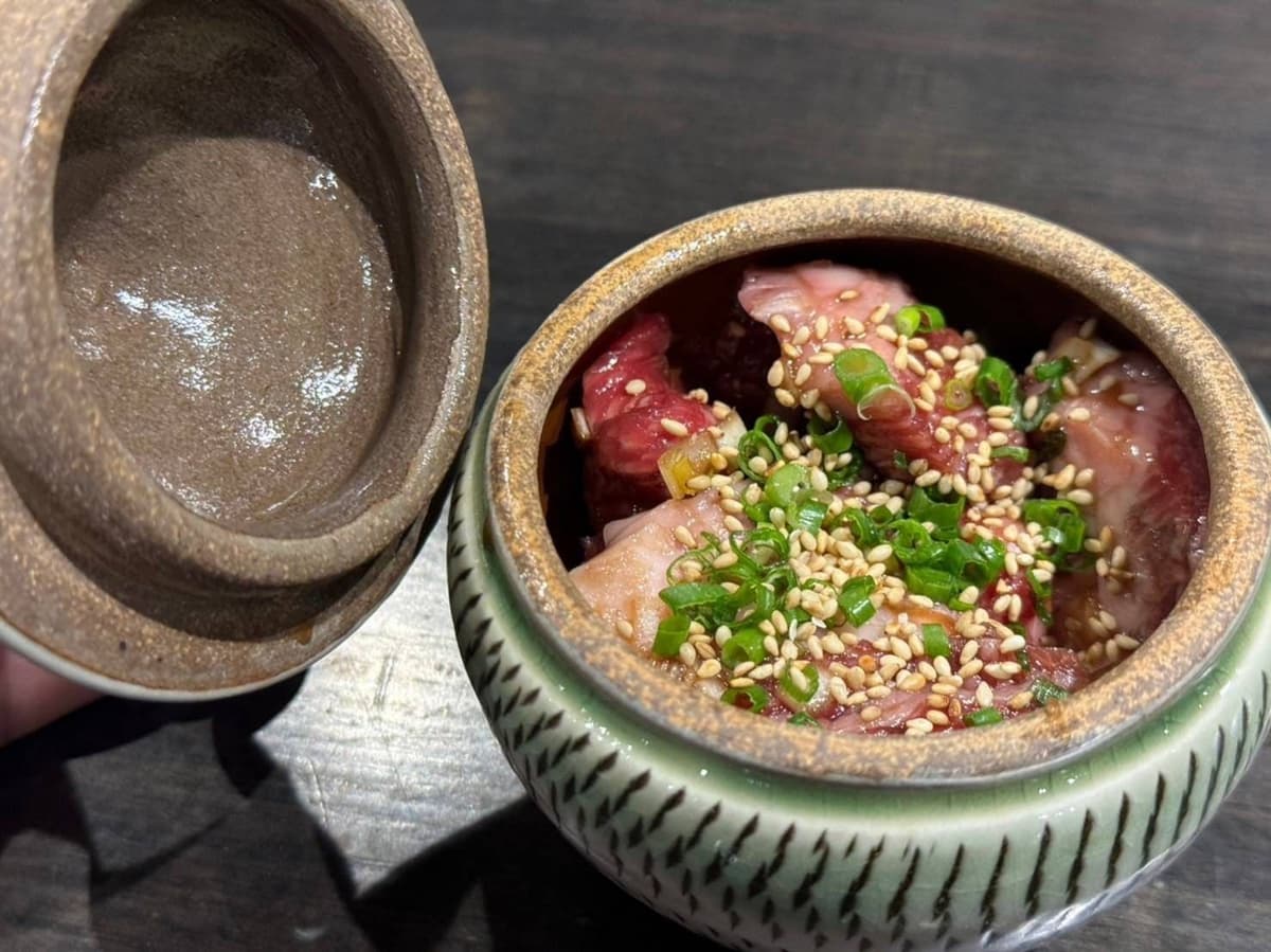 薬味のネギとゴマをのせた味付け肉が入った蓋付きの器