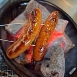 炭火の焼き網で香ばしく焼かれる2本のソーセージ