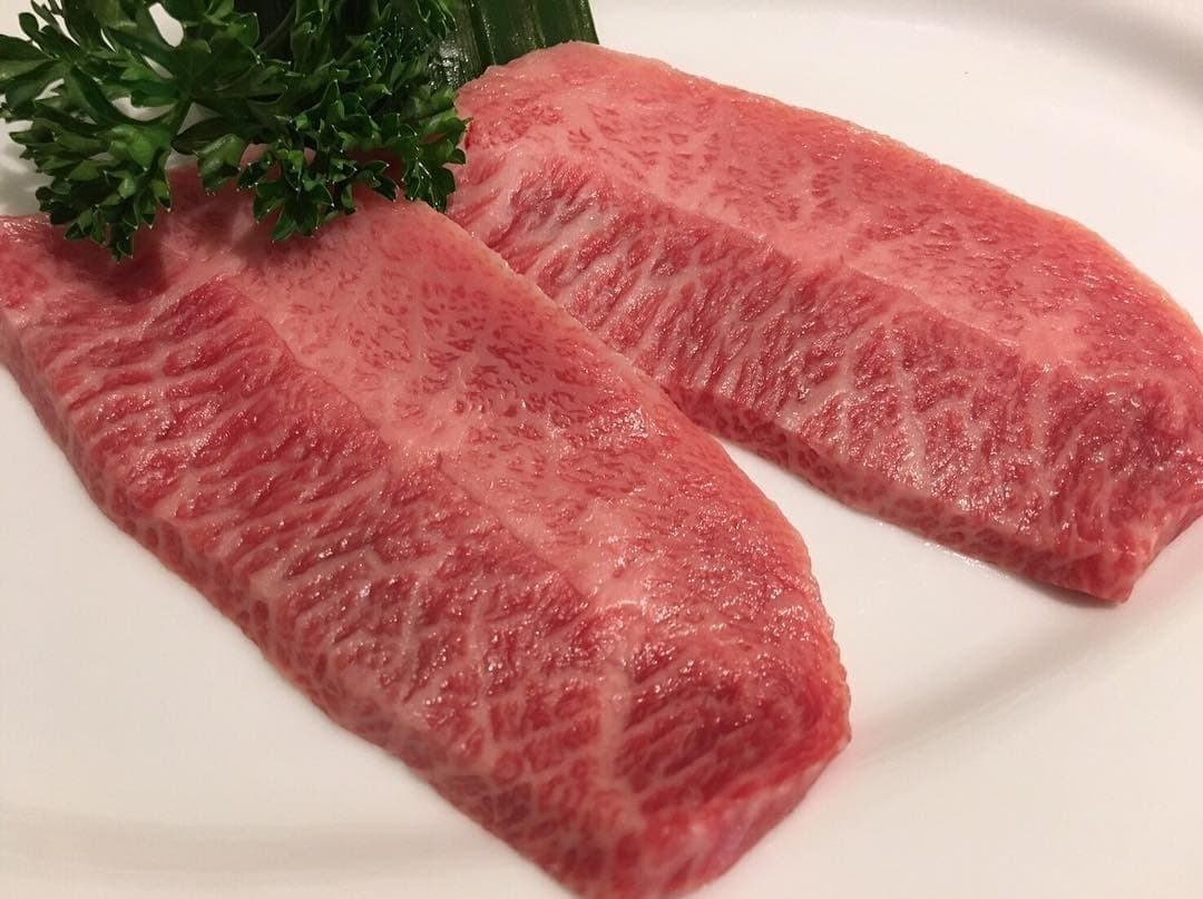 白い皿に盛り付けられた厚切りの霜降り牛肉2枚とパセリ添え