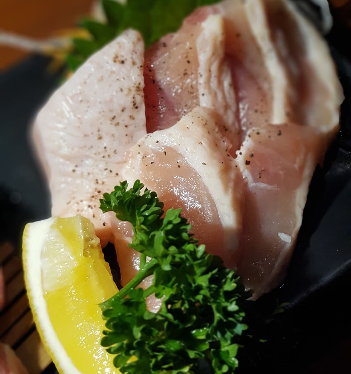 レモンとパセリを添えた、黒い器の鶏肉または白身肉の一皿
