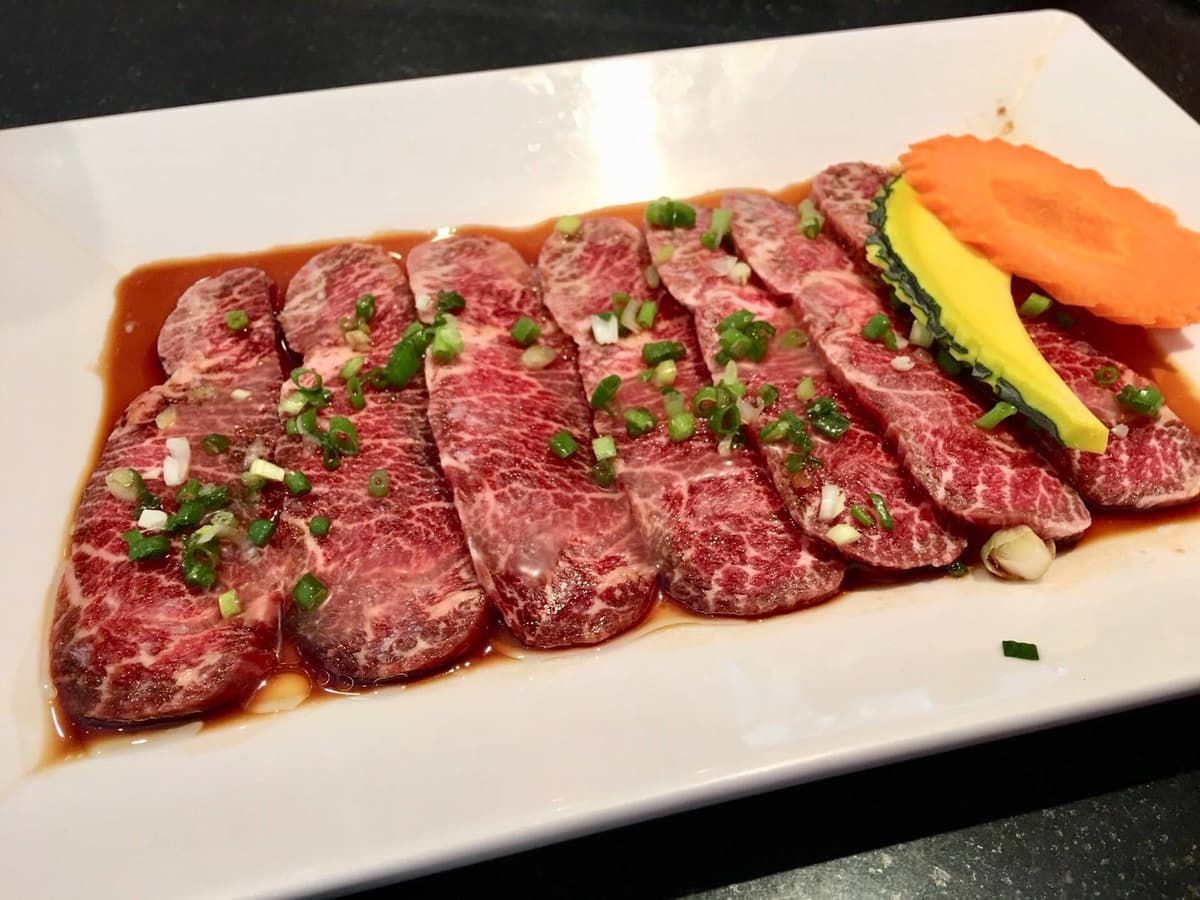 タレに漬けた薄切り牛肉を白い皿に盛り、ネギと野菜を添えた焼肉メニュー