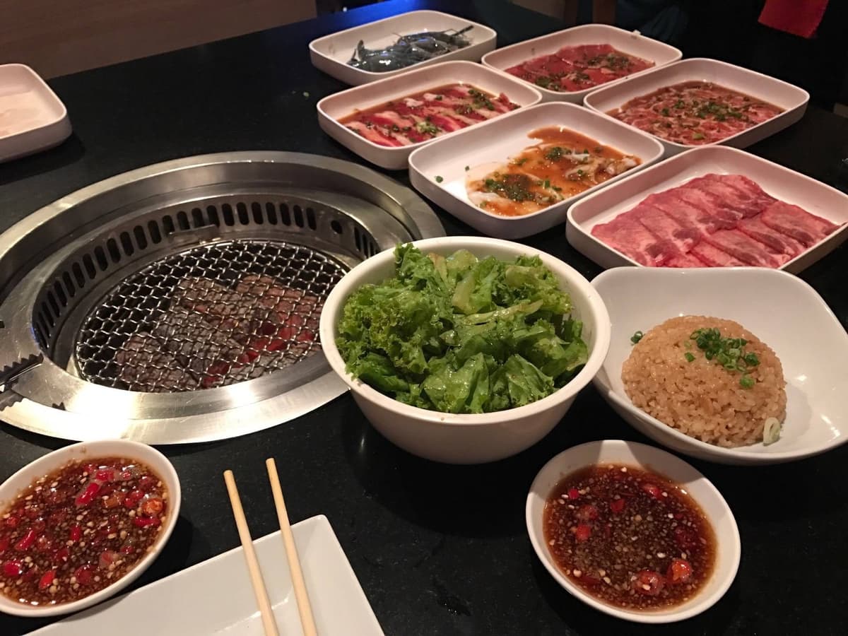 卓上ロースターの周りに肉、海鮮、サラダ、ガーリックライス、タレを並べた焼肉セット