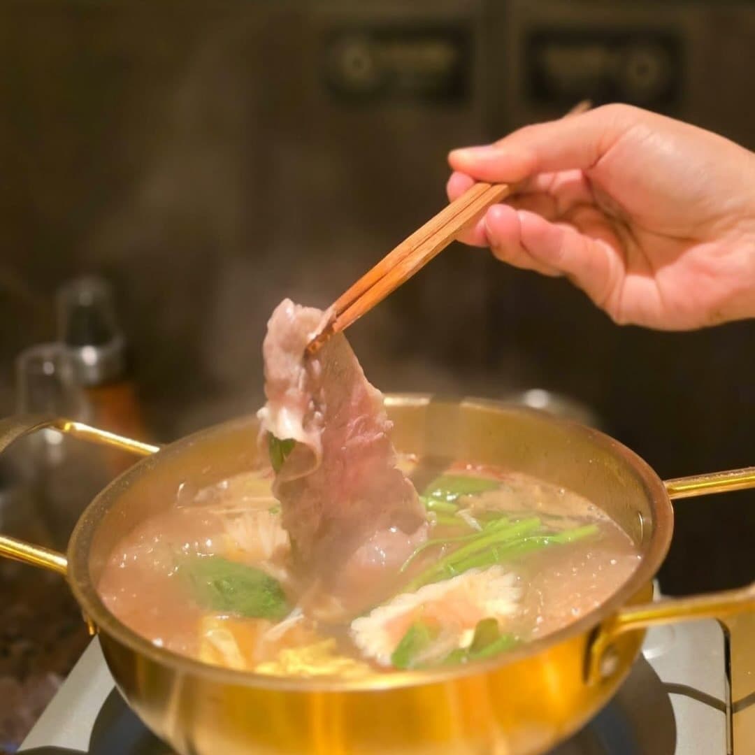金色の鍋でしゃぶしゃぶしている薄切り肉を箸で持ち上げる様子