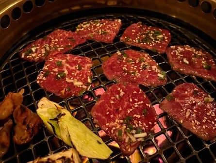 網の上でネギやゴマが振られた薄切りの牛肉が焼かれている様子。