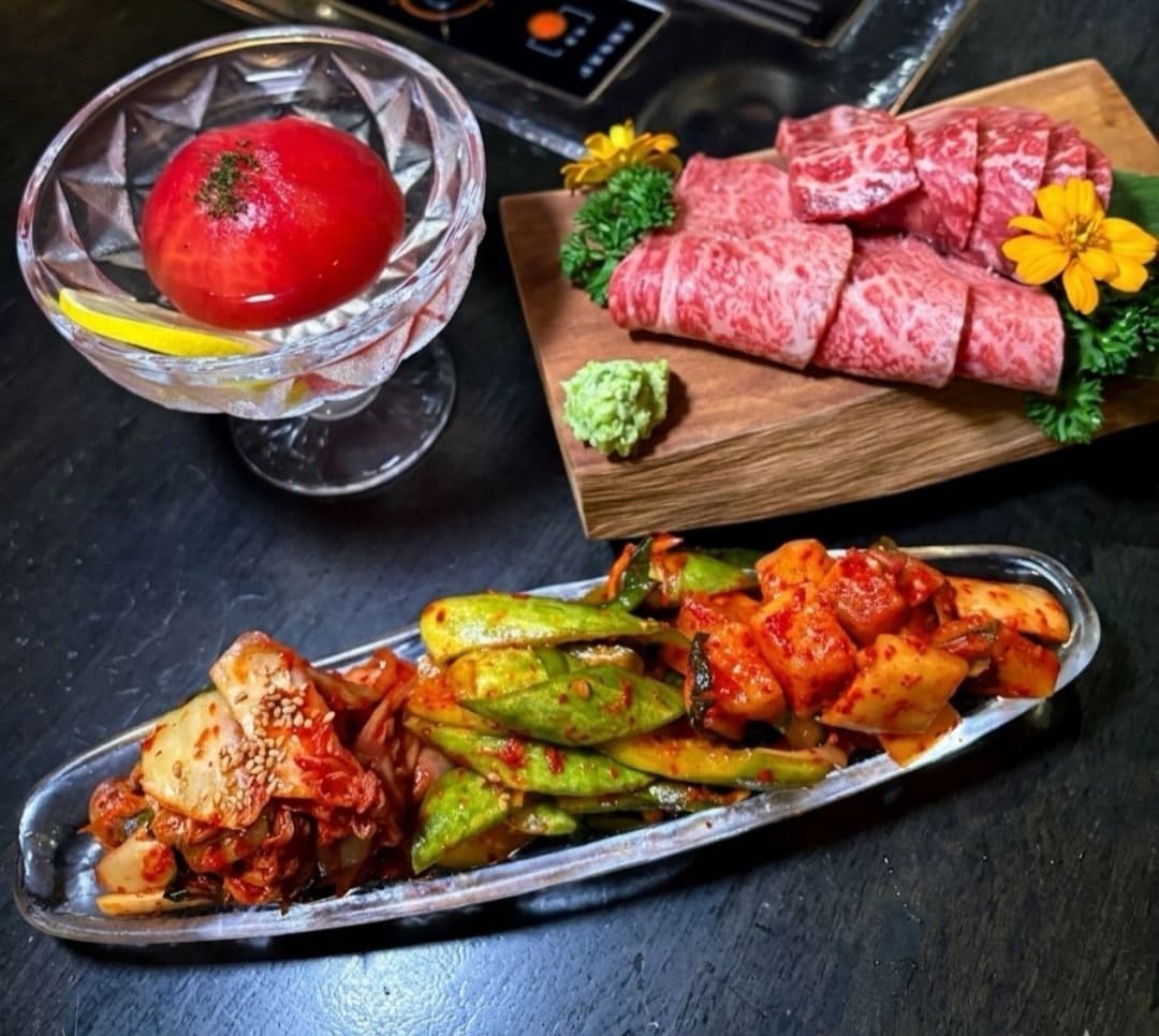 ロースター付きのテーブルに並ぶ焼肉のサイドメニューと肉。