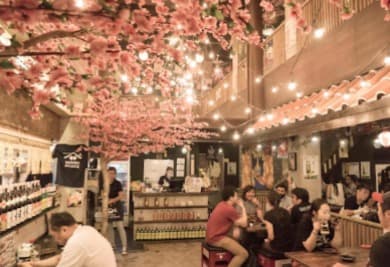 満開の桜の装飾とレトロなポスターが懐かしい、仕事帰りの熱気に満ちた「剣心 居酒屋」のフロア