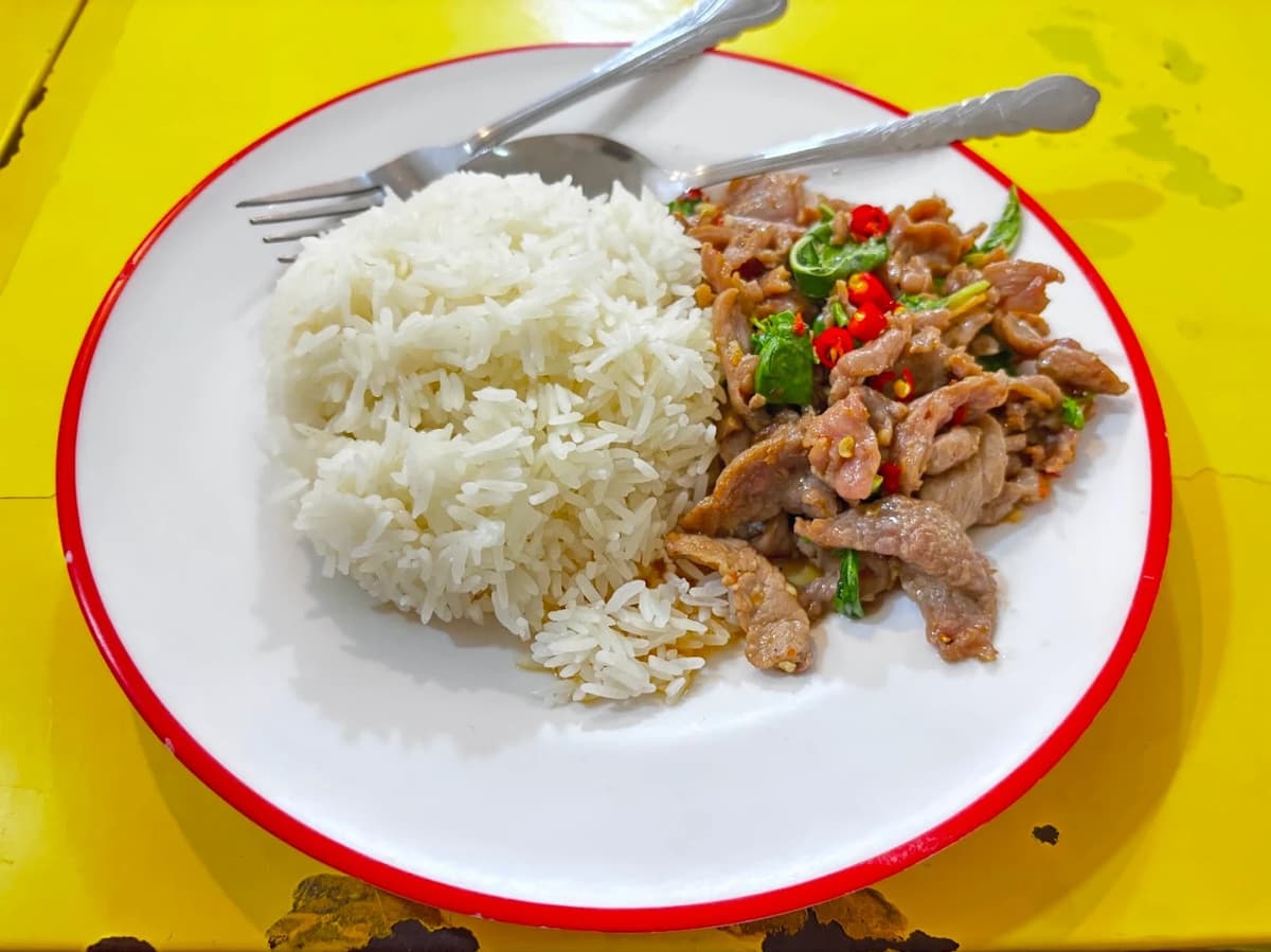 黄色のテーブルの上に置かれた、赤フチの白いお皿に盛られたご飯と豚肉の唐辛子炒め。