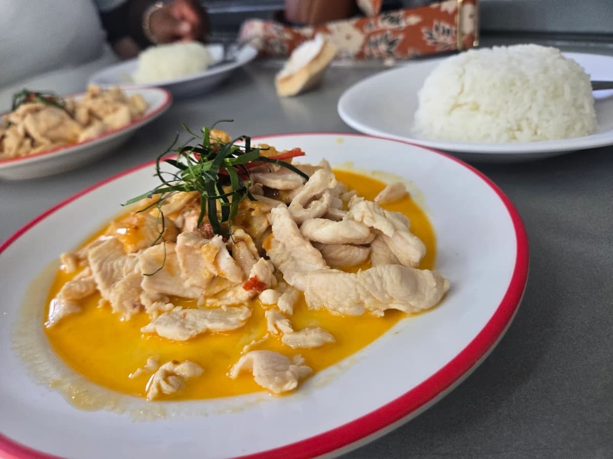 赤フチの白いお皿に盛り付けられた、鮮やかな黄色いソースと鶏肉の炒め物。