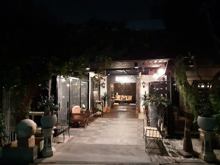 夜の静かな一軒家レストランの入り口で、タイルのアプローチの先にソファや温かい照明が見える様子。