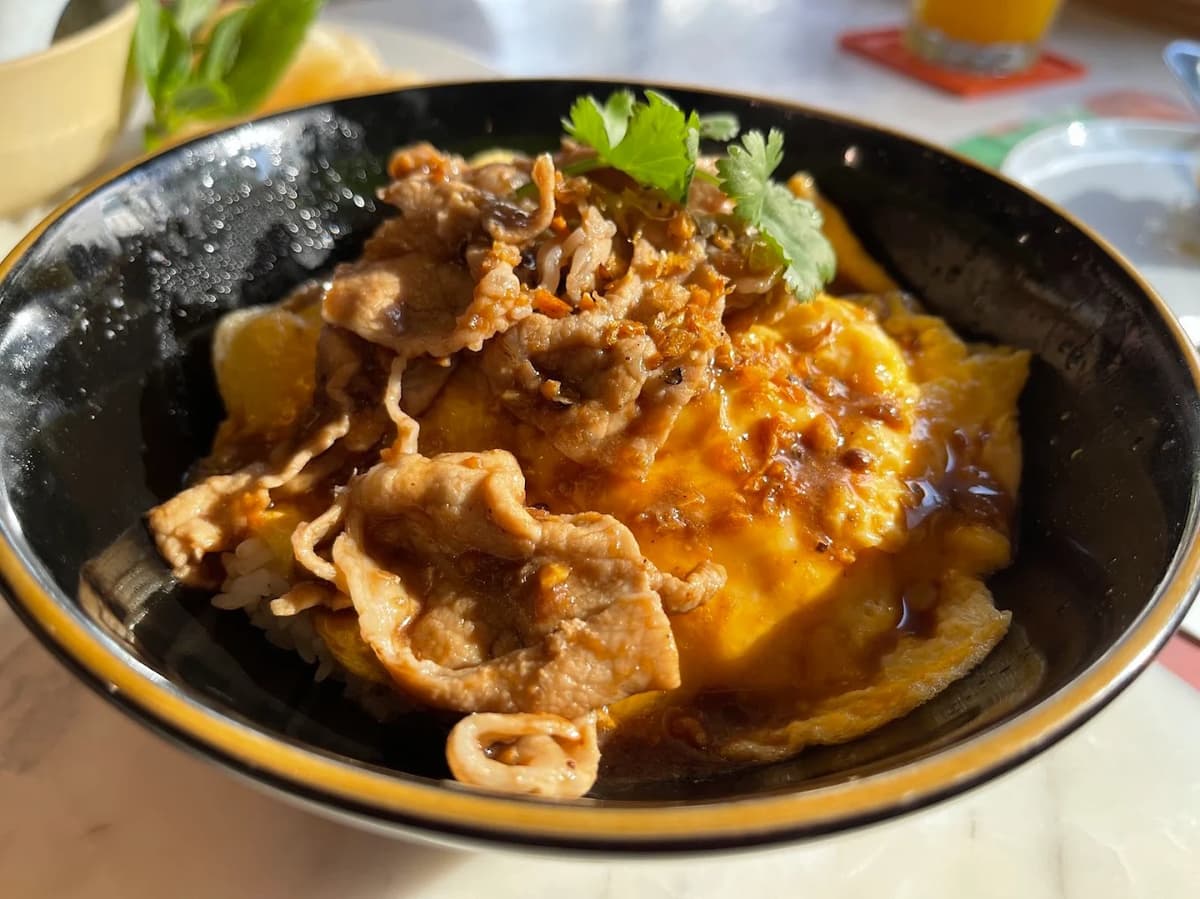 とろっとした卵焼きの上に、甘辛く炒めた薄切りの豚肉とパクチーがトッピングされた丼料理。