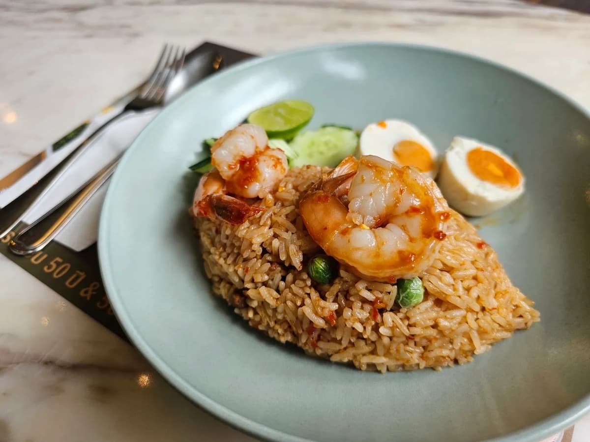 綺麗に型取られた大きなエビのチャーハン(カオパット)の皿。付け合わせにライム、キュウリ、塩漬け卵が添えられている。