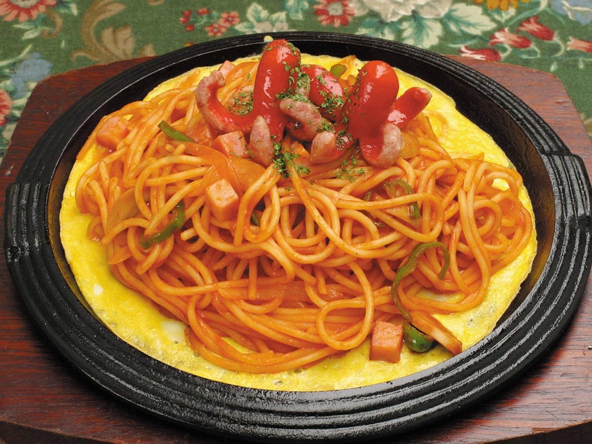 熱々の鉄板の上に薄焼き卵が敷かれ、その上にたっぷりと盛られたナポリタンスパゲティ。トッピングに赤いウインナーがのっている。