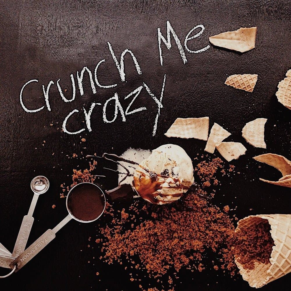 「Crunch Me Crazy」と書かれた黒いテーブルにアイスクリームやワッフルコーンを並べたイメージ