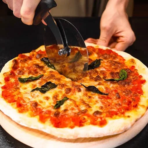 ピザカッターで切り分ける、バジルとチーズをのせた焼きたてピザ